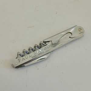 May include: Silver-toned bottle opener with a corkscrew and a label that reads "Paul Masson Vineyards".