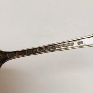 May include: Close-up of a silver spoon with the text "OLD COMPANY PLATE" and the initials "W.M.P." stamped on the handle. The spoon has a vintage look.