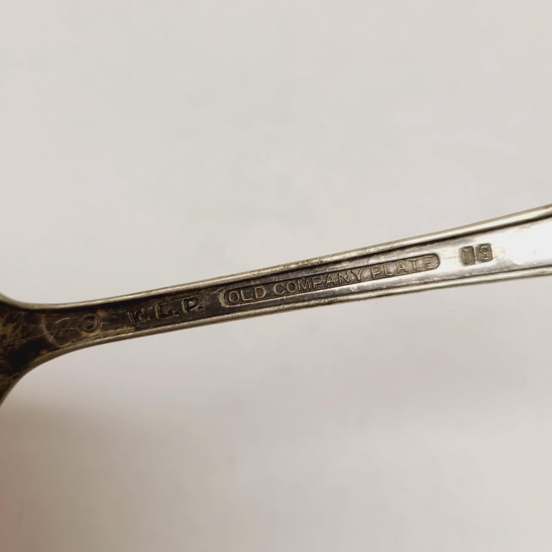 May include: Close-up of a silver spoon with the text "OLD COMPANY PLATE" and the initials "W.M.P." stamped on the handle. The spoon has a vintage look.