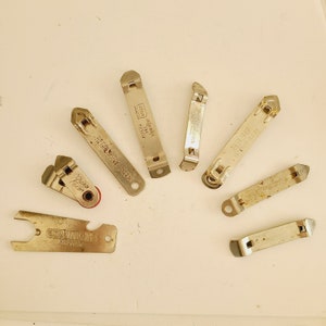 May include: A collection of vintage metal bottle openers in various shapes and sizes. Some openers have text, including "Regal Pale Beer", "Let's Open It", and "Simmons Unher". The openers are silver and show signs of age and use.