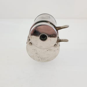 Puede incluir: Un sacapuntas de plata con un ojo de cerradura y una palanca a cada lado. El sacapuntas tiene el texto "J.D. FARE CO. TURNS" en la parte inferior.