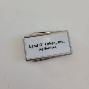 May include: A silver pocket knife with a white rectangular insert that says "Land O' Lakes, Inc. Ag Services".