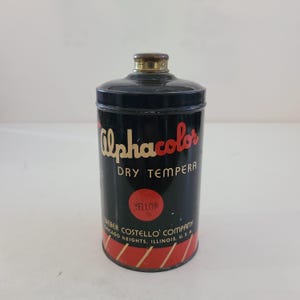 May include: A vintage tin of Alphacolor Dry Tempera paint in yellow. The tin is black with red and white stripes and the text "Alphacolor Dry Tempera" and "Weber Costello Company Chicago Heights, Illinois, U.S.A."