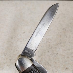 以下が含まれることがあります： 部分的に開いた銀色の刃のポケットナイフのクローズアップ。 刃はわずかに湾曲したエッジと尖った先端を持っています。 ハンドルは暗い色で、テクスチャパターンがあります。 テキスト「640045R」がブレードに表示されます。