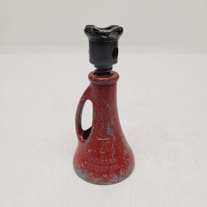 May include: A vintage red metal screw jack with a black top handle and a flared base. The red paint shows significant wear and chipping, revealing grey metal underneath. The body features the embossed text CHICAGO and DESIGN REG.