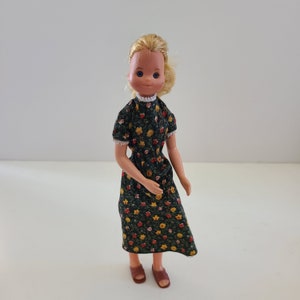 May include: A vintage doll with blonde hair wearing a green floral dress and brown shoes.