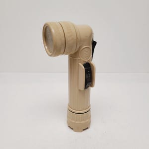 May include: Tan-colored, right-angle flashlight with a ribbed handle and a round, ridged head. The flashlight has a black on/off switch and a black clip. The model number "SX 991/0" is printed on the side.
