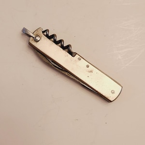 May include: A silver pocket knife with a corkscrew and a blade. The knife is closed and has a smooth, metallic finish.
