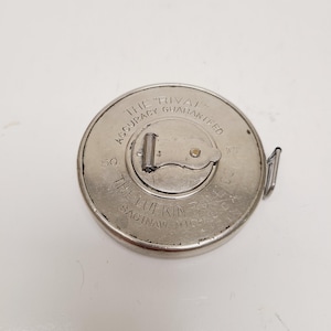 May include: A vintage silver metal Lufkin Rival measuring tape. The tape measure has the text "Accuracy Guaranteed" and "The Lufkin Rule Co. Saginaw, Mich." The tape measure is 50 feet long.