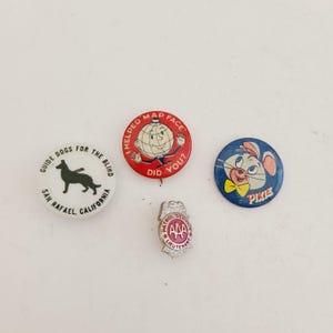 May include: A collection of vintage pins and a badge. The pins include a white pin with a black dog silhouette and text, a red pin with a globe character, and a blue pin with a cartoon mouse. A silver AAA badge is also present.