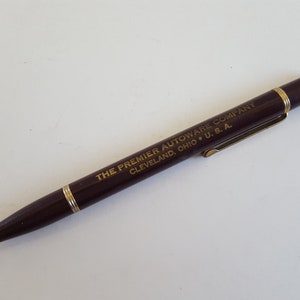 May include: A brown mechanical pencil with a gold-colored clip and a gold inscription that reads "THE PREMIER AUTOWARE COMPANY CLEVELAND, OHIO * U.S.A."