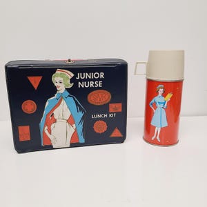 May include: A vintage Junior Nurse lunch kit and thermos set. The lunch kit is navy blue with a nurse illustration and the words "Junior Nurse" and "Lunch Kit". The thermos is red with a nurse illustration and a beige lid.