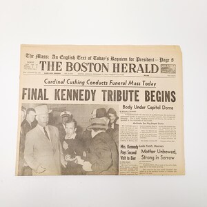 May include: A vintage copy of The Boston Herald newspaper from November 25, 1963, with the headline "Final Kennedy Tribute Begins." The front page features a black and white photograph and text about the funeral mass.