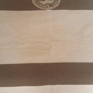 May include: A brown and tan striped blanket with a circular emblem in the top left corner. The emblem features a white eagle with a shield and the text "Veterans Administration".