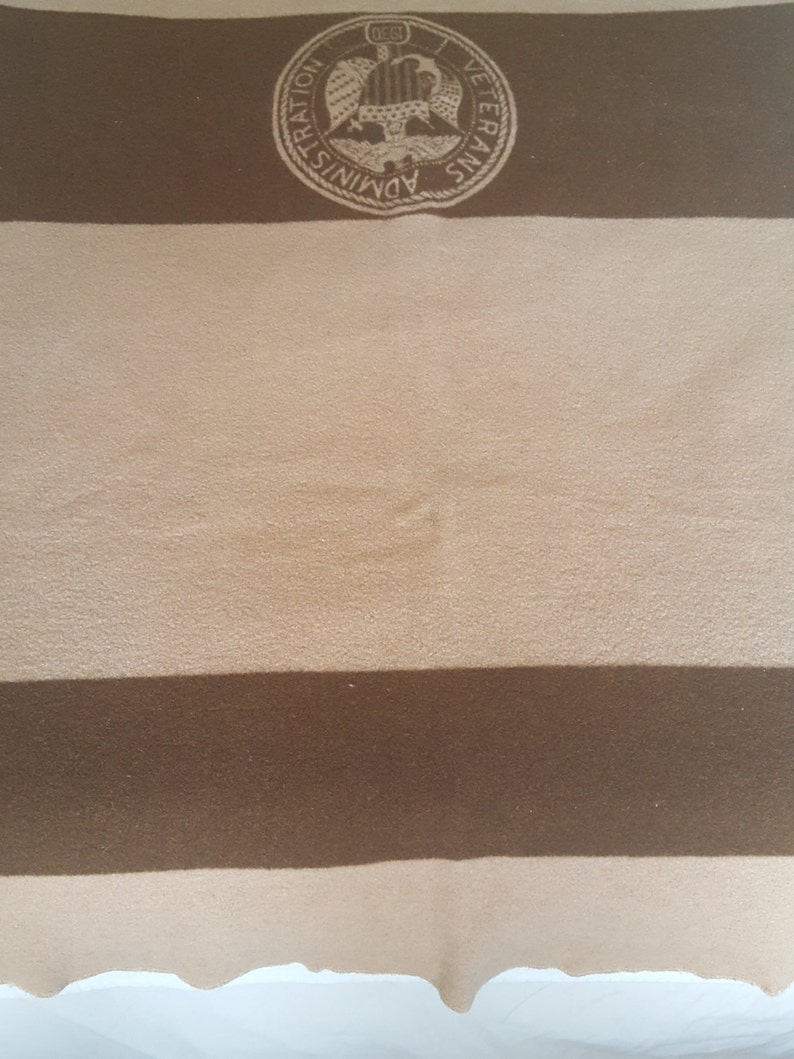 May include: A brown and tan striped blanket with a circular emblem in the top left corner. The emblem features a white eagle with a shield and the text "Veterans Administration".