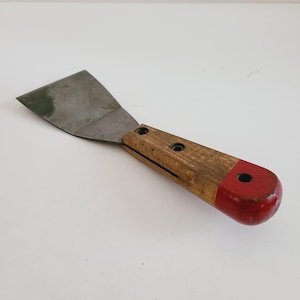 May include: A metal putty knife with a wooden handle. The handle is painted red at the end.