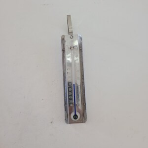 May include: A silver candy thermometer with a blue indicator needle. The thermometer has a range of 30 to 180 degrees Fahrenheit. It is made in the USA.