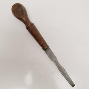 May include: A vintage wood-handled chisel with a metal blade. The handle is a dark brown color, and the blade is a dull silver. The chisel is designed for woodworking and has a classic, well-worn appearance.