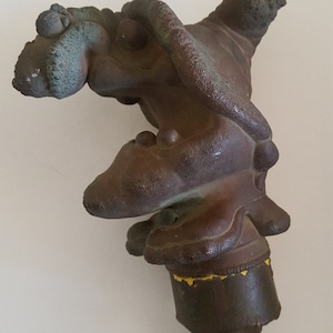 May include: A brown, textured, abstract sculpture with a yellow base. The sculpture has a unique, organic shape and appears to be made of metal.