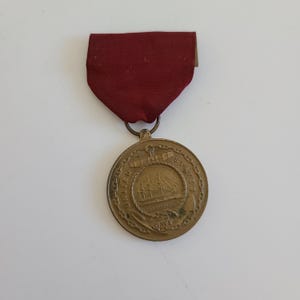 May include: A gold medal with a red ribbon. The medal features a ship with the words "United States Navy" around the edge.