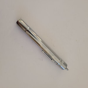 May include: A silver metal flashlight with a long, slender design. The flashlight has a smooth, polished finish and a small button on the side.