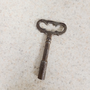 May include: An antique, rusty metal key with a distinctive three-lobed handle. The key's stem is cylindrical, and the handle has a decorative, open design. The key shows signs of age and wear, suggesting it is a vintage item.