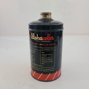 May include: A vintage tin of Alphacolor Dry Tempera paint. The tin is black with red and white lettering. The text on the tin reads "Alphacolor Dry Tempera The Brightest Name in Color". The tin also includes instructions for mixing the paint with water, textile liquid, oil, varnish, and a finishing paint.