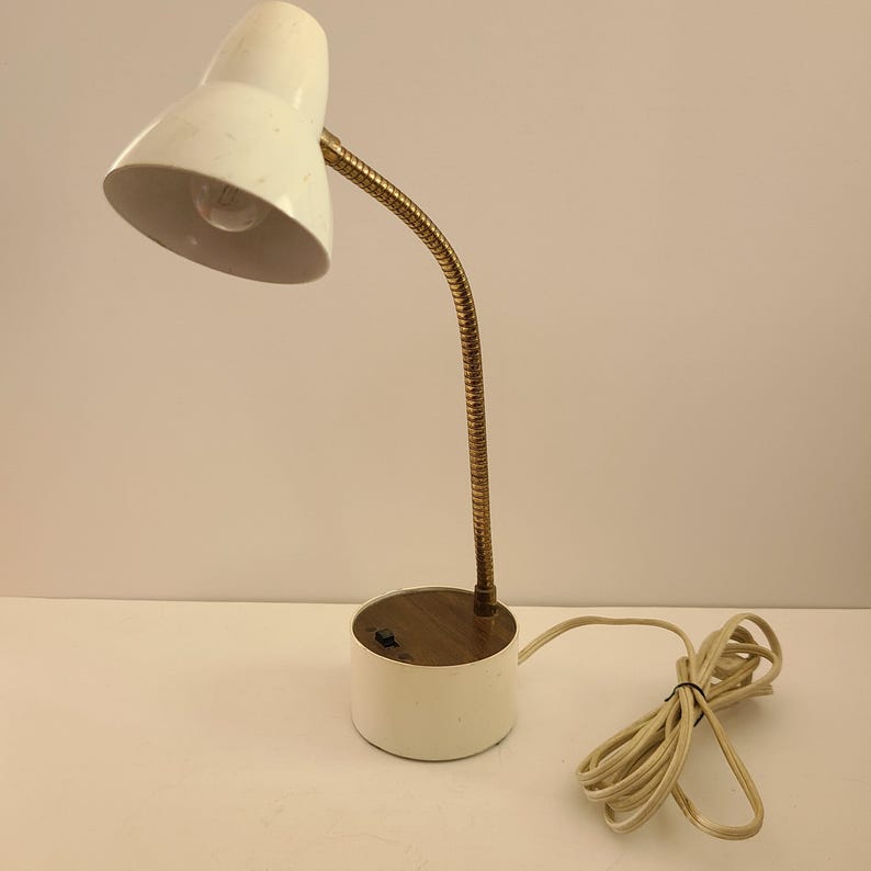 May include: A vintage white desk lamp with a flexible brass neck and a round base. The lamp has a classic design with a white lampshade and a cord. The lamp is approximately 12 inches tall.