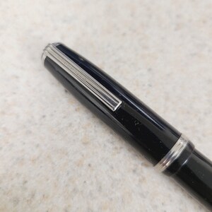 May include: Close-up of a black fountain pen with silver accents. The pen has a shiny, polished finish and a silver clip. The pen is lying on a light-colored surface.