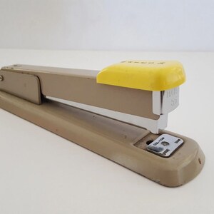 May include: A beige metal stapler with a yellow top and a silver staple remover. The stapler has the text "Swingline 50" printed on the side.