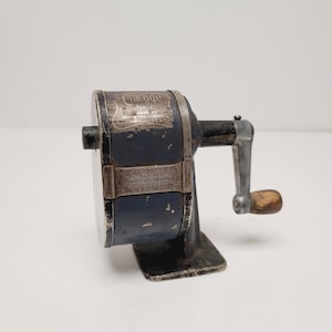 May include: An antique Chicago No. 2 Automatic Pencil Sharpener. The sharpener is dark blue with silver accents and a wooden handle. The text "Chicago" and "Automatic Pencil Sharpener" are visible.