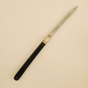 May include: A vintage letter opener with a long, slender, stainless steel blade. The handle is black with brass rivets and a silver-colored metal bolster. The opener is designed for slicing open envelopes and other paper items.