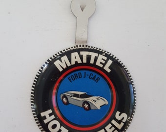 Può includere: Un bottone rotondo bianco e nero Hot Wheels con un bordo rosso e bianco. Il bottone presenta una Ford J-Car bianca su uno sfondo blu. Il testo "MATTEL" è stampato in bianco su uno sfondo nero. Il testo "FORD J-CAR" è stampato in bianco su uno sfondo rosso. Il testo "HOT WHEELS" è stampato in bianco su uno sfondo rosso. Il testo "C1967 Mattel Inc. Hong Kong" è stampato in nero su uno sfondo bianco.