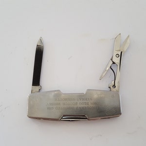Op de afbeelding: Een zilveren multitool met een mes, een schaar en andere gereedschappen. De tool is gegraveerd met de tekst "AVONDA  PATENTED  USA  MINI  EDC  TOOL  WHITNEY  ILLINOIS".