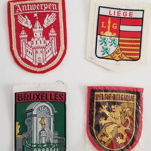 May include: Four embroidered patches featuring city names. One red patch says "Antwerpen" with a castle design. Another says "Liege" with a coat of arms. A third says "Bruxelles" with a fountain. The last says "Belgie-Belgique" with a lion.