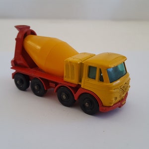 May include: A yellow and red toy cement mixer truck with a rotating drum. The truck has four wheels and a detailed cab.
