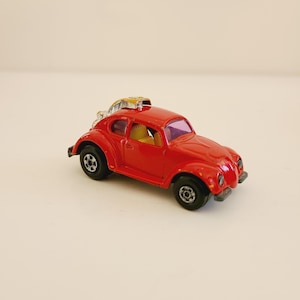May include: A small, red toy car with black wheels and a yellow interior. The car has a silver and yellow accessory on the roof. The toy car is a classic design, likely a vintage collectible.