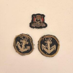 May include: Three embroidered patches, one with a crown and two with anchors. The patches are black with gold embroidery.