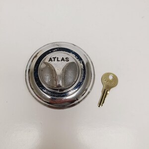 May include: A chrome-plated gas cap with the word "ATLAS" and a small brass key with "GAS" printed on it. The gas cap has a unique design with two raised sections. The key is small and has a simple design.