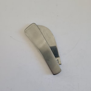 May include: A silver-colored money clip with a curved design. The clip is made of a shiny metal and has a rectangular shape on the ends. The clip is slightly open, revealing the inside.