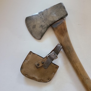 May include: A vintage axe with a wooden handle and a leather sheath. The axe head is made of metal and has a slight curve to the blade.