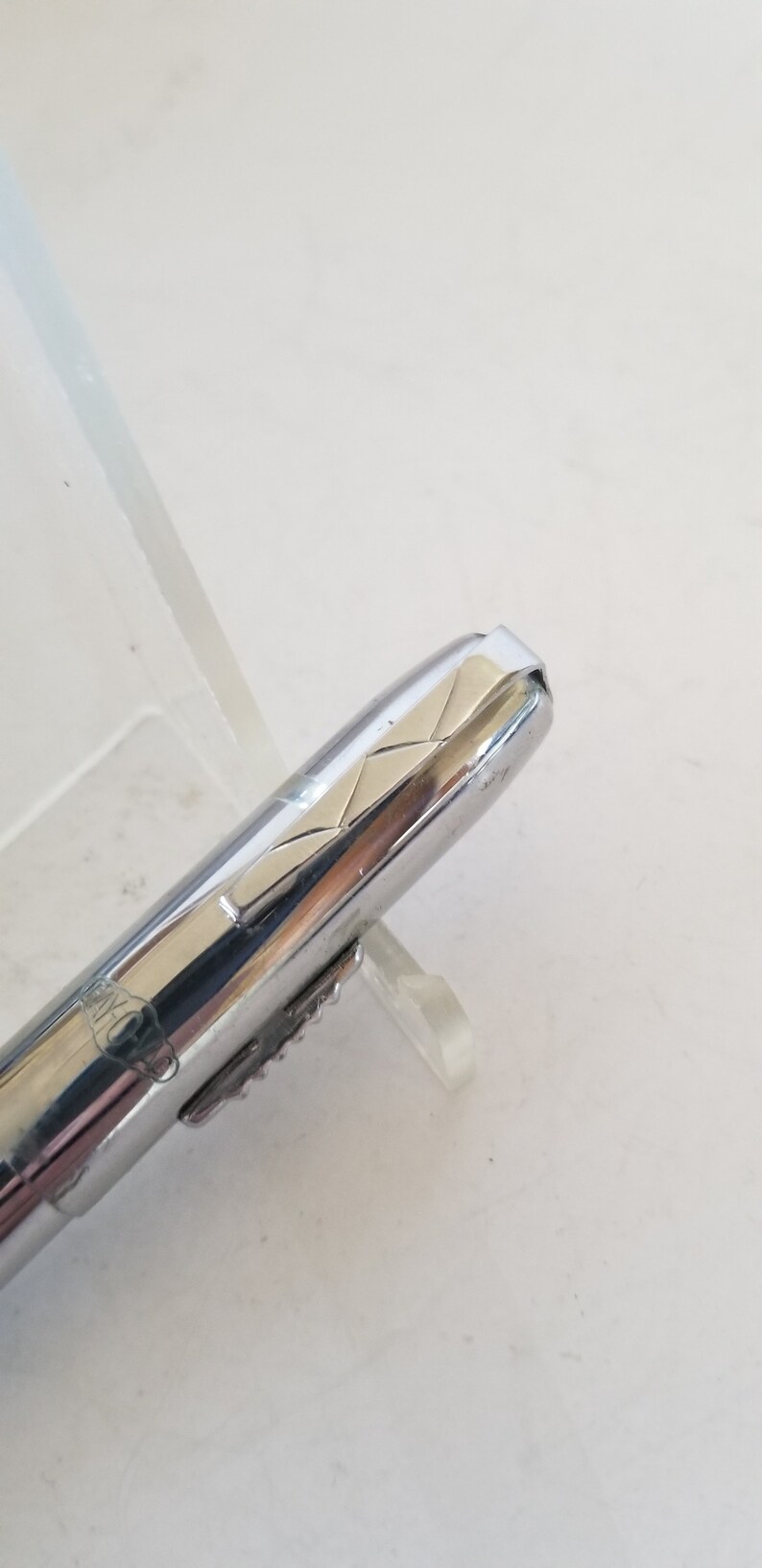 Peut inclure: Un stylo argent&eacute; et dor&eacute; avec un motif textur&eacute; sur le capuchon. Le stylo est sur une surface blanche.