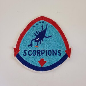 May include: A blue and red embroidered patch with a scorpion design and the text "SCORPIONS".