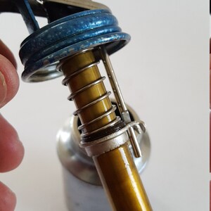 Puede incluir: Primer plano de una lata de aceite vintage con tapa azul y boquilla dorada. La boquilla tiene un resorte y un clip met&aacute;lico.