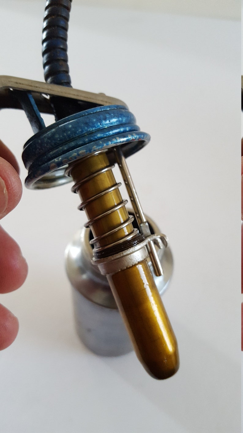 Puede incluir: Primer plano de una lata de aceite vintage con tapa azul y boquilla dorada. La boquilla tiene un resorte y un clip met&aacute;lico.
