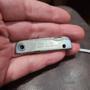 May include: A silver multi-tool with a black handle. The tool has a variety of blades and tools, including a knife, a screwdriver, and a file. The tool is engraved with the words "Tops in Tools" and "Quality - Price - Service".