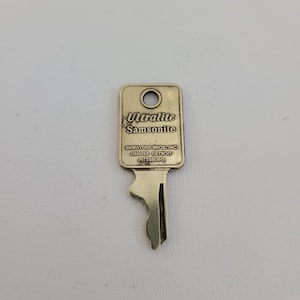 May include: A gold-colored metal key with the words "Ultralite Samsonite" and "Shwayder Bros. Inc. Denver Detroit Pittsburg" engraved on the top.