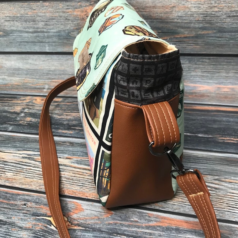 May include: A brown leather crossbody bag with a flap closure and a patterned fabric lining. The bag has a long adjustable strap and a metal clasp.