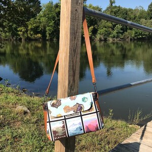 May include: A brown leather shoulder bag with a colorful fabric flap featuring images of national parks, including "Grand Canyon", "Glacier", and "Yosemite".