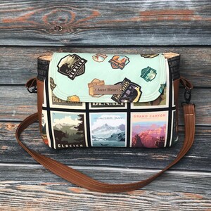 May include: A brown leather crossbody bag with a black and white fabric featuring images of national parks and the text "Aunt Henri".